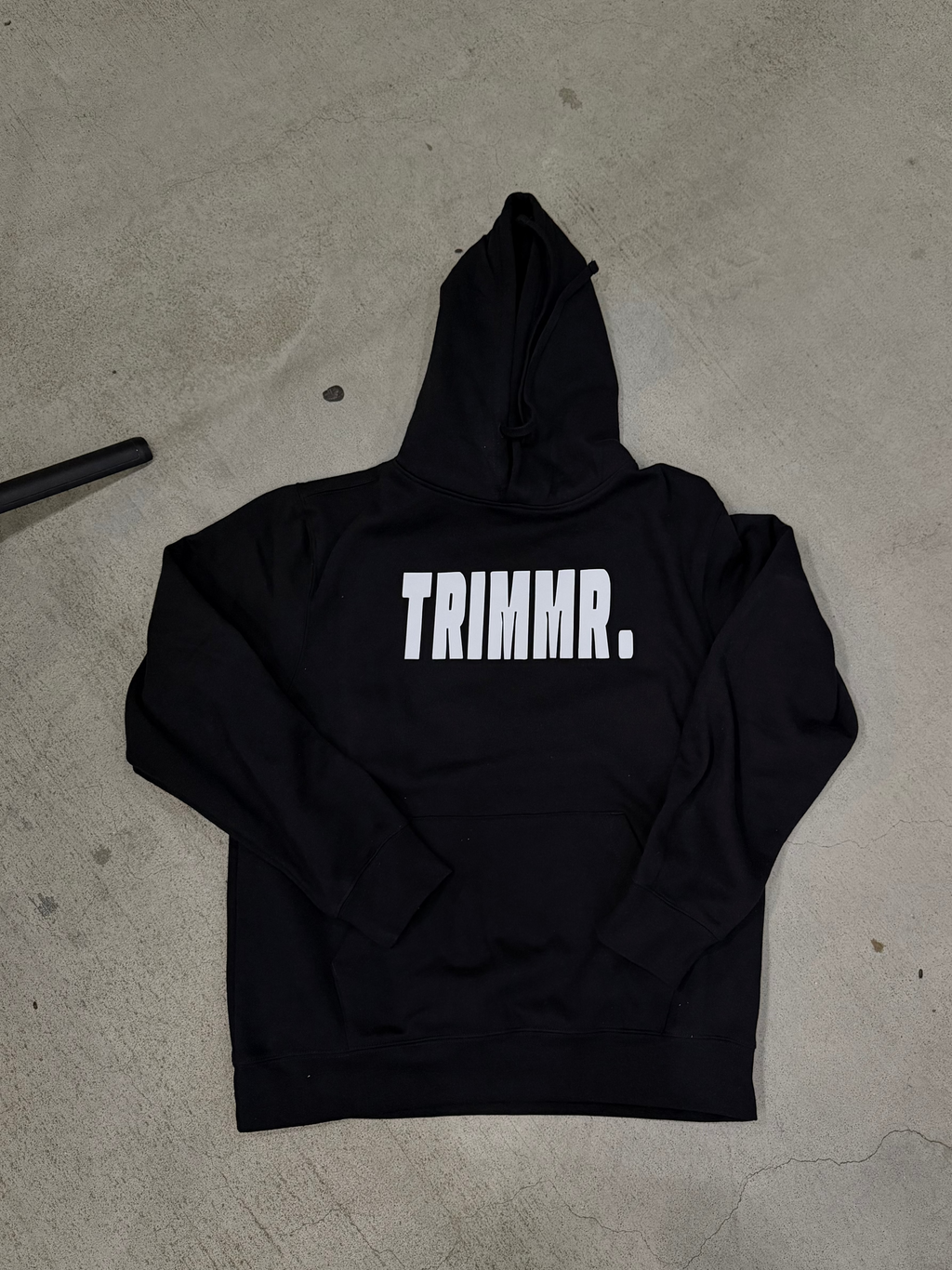 Black hoodie with 'TRIMMR.' text on a concrete floor